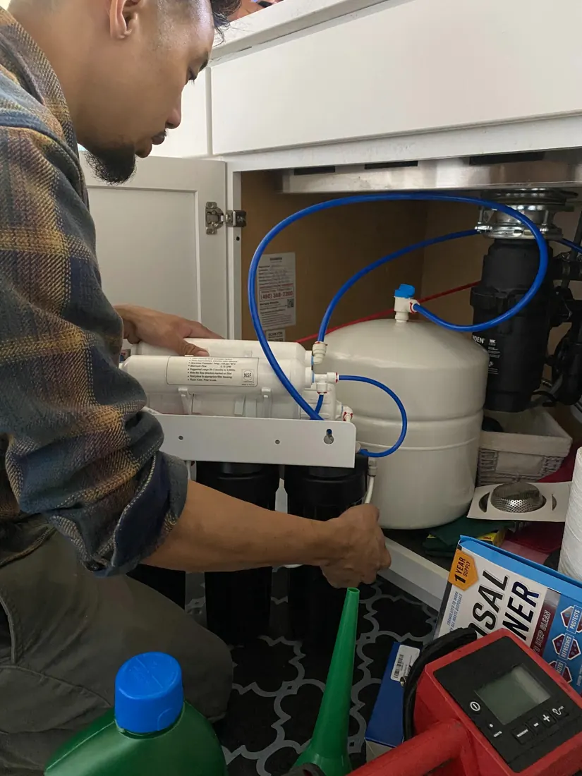Technician working on a reverse osmosis system beneath a kitchen sink